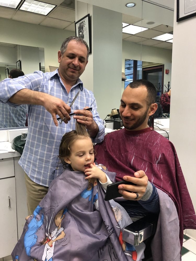 Barber cutting a toddler's hair while the father holds him in the chair