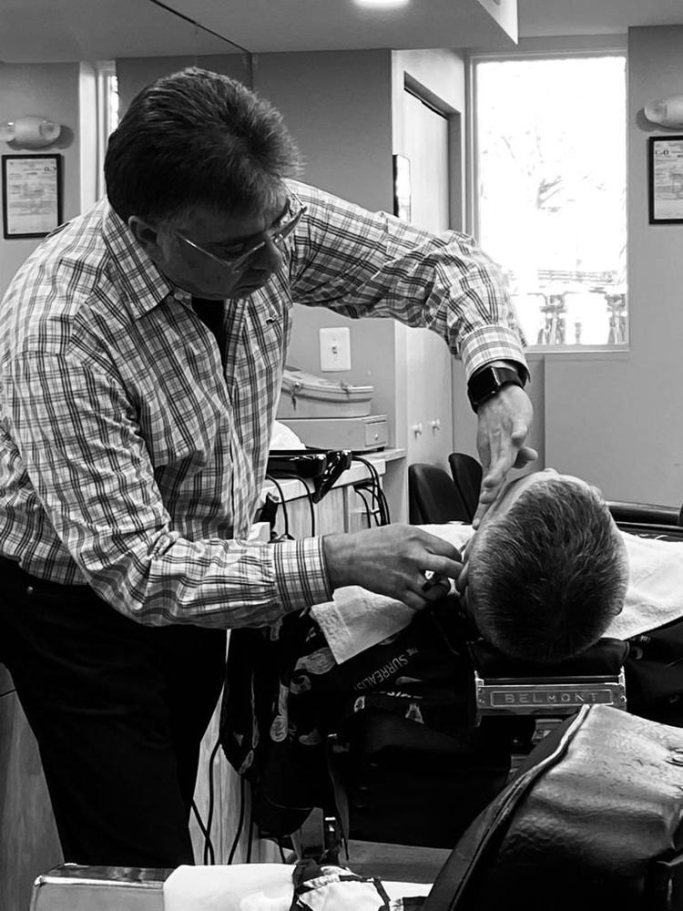 José Domingos, en noir et blanc, penché sur un client dans le fauteuil près de la fenêtre