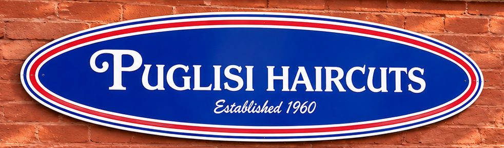 Oval blue Puglisi HairCuts sign, Established 1960, with red and white stripes, mounted on red brick
