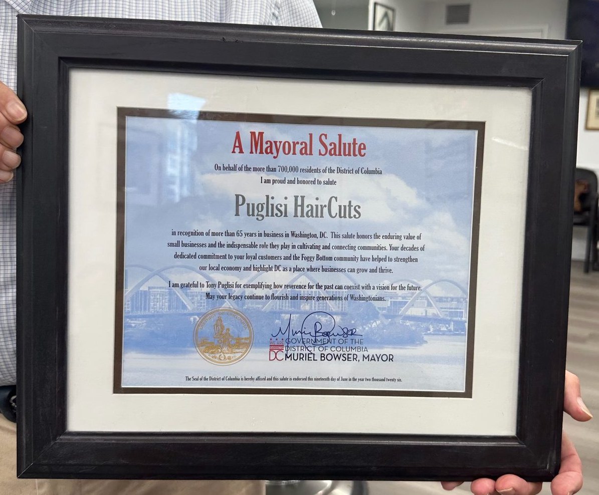 Tony Puglisi holding a framed Mayoral Salute to Puglisi HairCuts from Muriel Bowser
