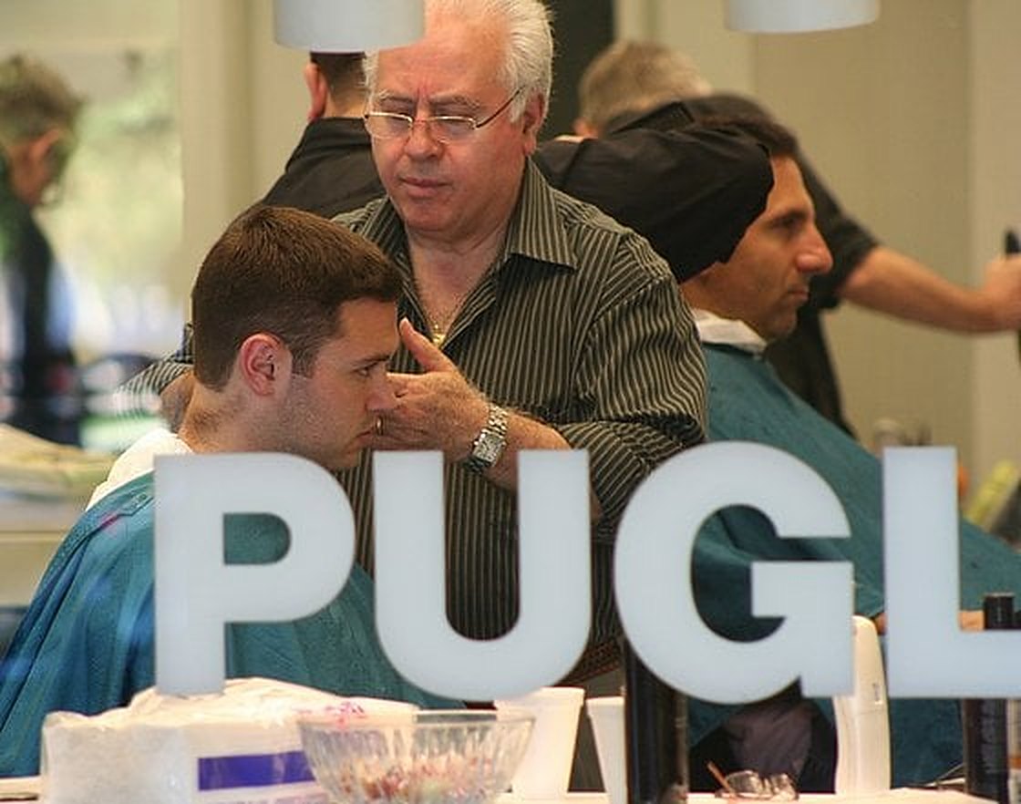 Las letras PUGL en el espejo mientras dos barberos cortan el pelo detrás