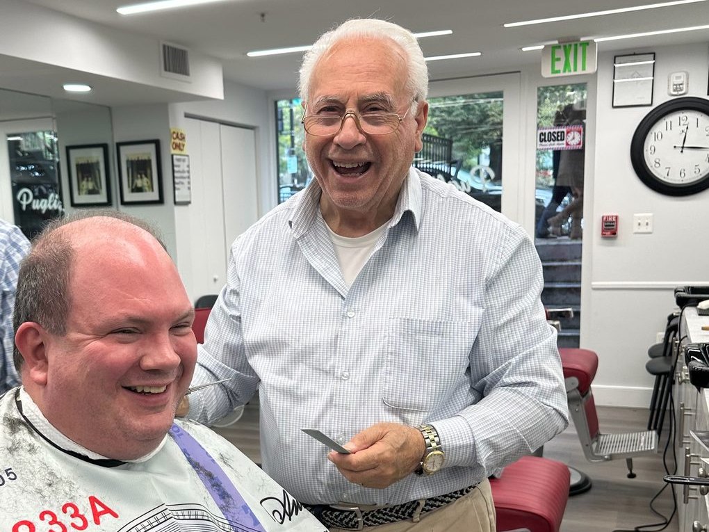 Tony Puglisi laughing beside a customer in the chair, October 2026